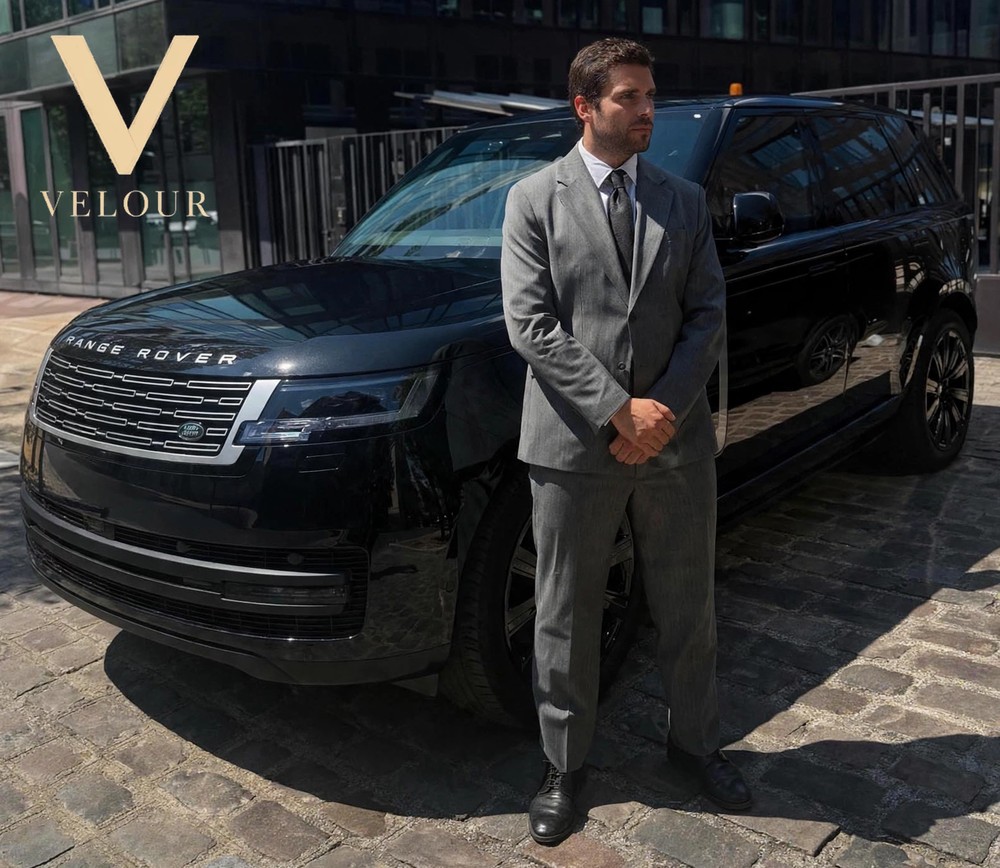 Chauffeur Velour en costume, en attente devant un Range Rover Vogue SV